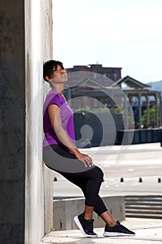 Full length side of young african woman leaning to wall outdoors after workout