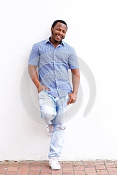 Full length smiling african american guy leaning against white wall