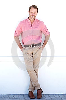 Full length smiling older man leaning against white wall