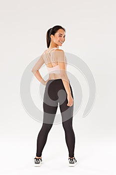 Full length of smiling slim and strong female fitness coach, female athelte in sportswear turn behind to look at camera