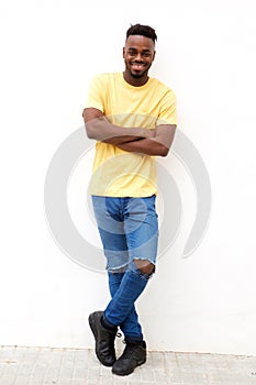 Full length smiling young black man leaning against white wall