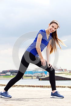 Full length smiling young sporty woman stretching outside