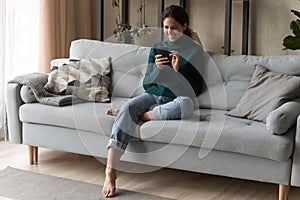 Full length smiling young woman using phone, relaxing on couch