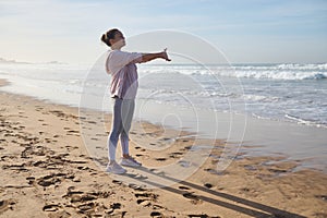 Full length sporty woman in activewear exercising on the beach, stretching and warming up her body before morning jog