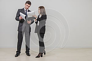 Full-length successful businesspartners standing, holding clipboards, flipping over pages, looking through the documents