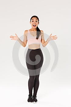 Full length of surprised and amazed female athelte, asian fitness girl in sportsbra and leggings looking wondered