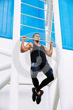 Full length view of confident sportsman doing pull ups, outdoors