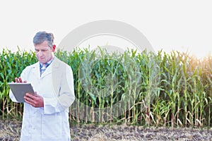 Full length view of crop scientist wearing lab coat while using digital tablet against corn plant growing in field photo