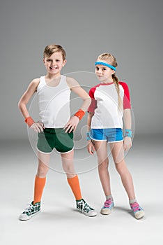 Full length view of cute smiling boy and girl in sportswear standing together on grey