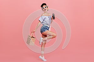 Full length view of dancing pinup girl. Studio shot of graceful young woman with bottle of beverage and bag