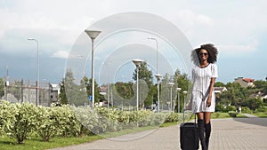 Full-length view of elegant smiling african american business lady with sunglasses going to the airport with her luggage