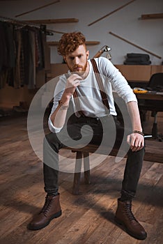 full length view of handsome stylish young male fashion designer sitting and looking