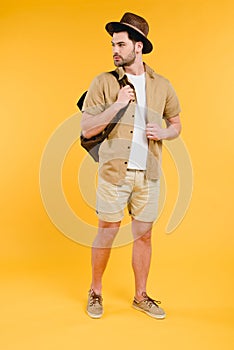 full length view of handsome young man in shorts and hat holding backpack and looking away