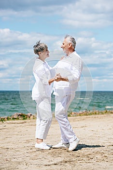 full length view of happy senior couple looking at each other while dancing at beach.