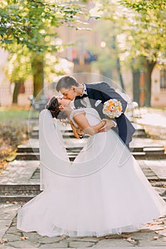 The full-length view of the kissing newlyweds at the background of the park.