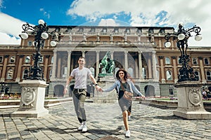 Full-length view of the pretty young couple in love holding hands while walking along the countryard at the Buda Castle photo