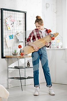 Full length view of teenager in jeans holding longboard at home.