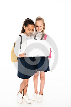full length view of two multicultural schoolgirls using laptop isolated on white.
