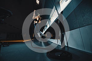 Full length wide angle shot of a woman performing rope climbs at the gym