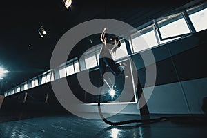 Full length wide angle shot of a woman performing rope climbs at the gym