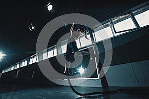 Full length wide angle shot of a woman performing rope climbs at the gym