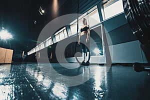 Full length wide angle shot of a woman performing rope climbs at the gym