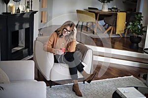 Happy woman using earphones and cellphone while sitting in an armchair at home