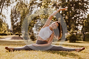 full length yoga concept. sporty slim woman in white t-shirt and grey leggins sit in yoga stretching slant position with