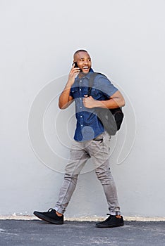 Full length young african man walking and talking on mobile phone