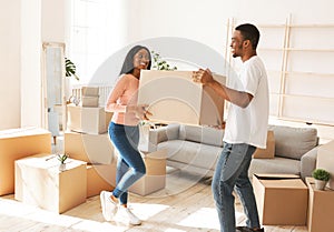 Full length of young black man with his girlfriend carrying cardboard box in their new home on moving day