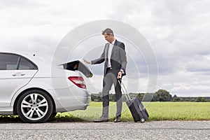 Full length of young businessman unloading luggage from broken down car at countryside