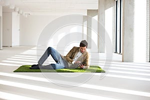 Full length of young businessman using digital tablet while reclining on turf in office