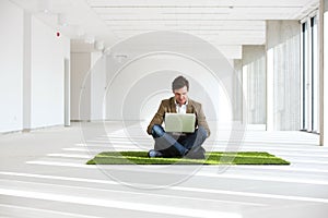 Full length of young businessman using laptop while sitting on turf in new office