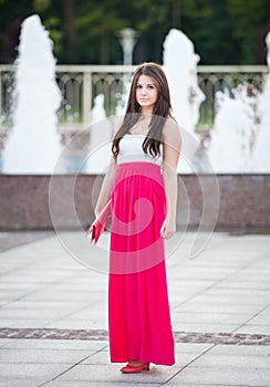 Full length of young caucasian female with long red skirt standing in front of a fountain outdoor