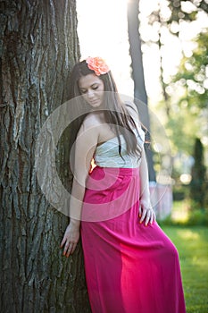 Full length of young caucasian female with long red skirt standing near the tree outdoor