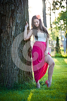 Full length of young caucasian female with long red skirt standing near the tree outdoor