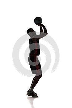 Full-length of young concentrated man, basketball player standing and throwing ball into basketball hoop isolated on