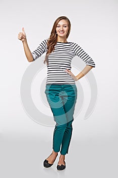 Full length of young cute smiling emotional girl giving you thumb up, on gray background