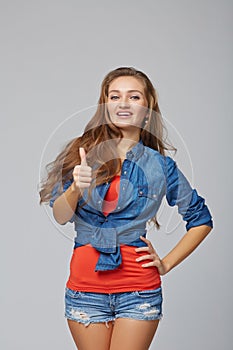 Full length of young cute smiling emotional girl giving you thumb up, on gray background