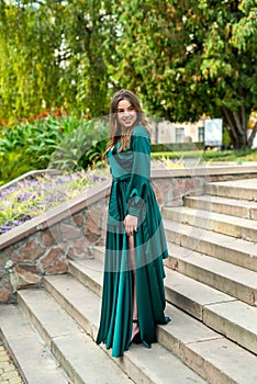 full length young elegant woman in beautiful green gress standing in stone stair