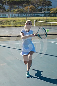 Full length of young female caucasian tennis player hitting ball with racket at court on sunny day