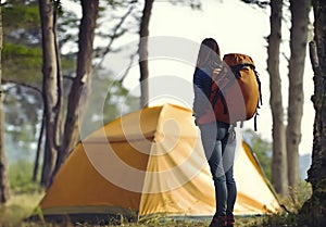 full length young girl female standing with big rucksack near toustic tent at summer forest park background. woman wearing jacket