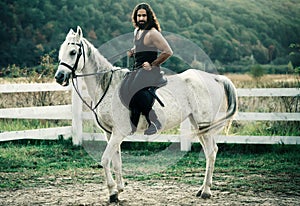 Full length of young handsome man sitting on his white stallion at the country side. Man equestrian on his horse riding