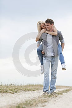Full length of young man giving piggyback ride to woman on trail at field