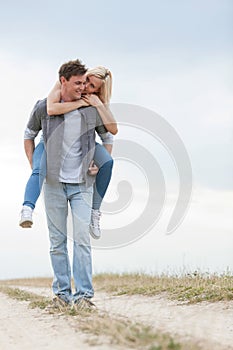 Full length of young man giving piggyback ride to woman on trail at field