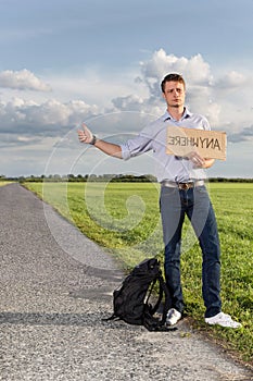 Full length of young man hitching while holding anywhere sign on countryside