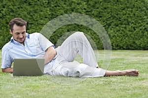 Full length of young man using laptop while lying on grass in park