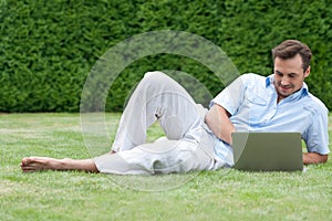 Full length of young man using laptop while lying on grass in park