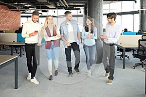 Full length of young people in smart casual wear discussing business and smiling while walking through the office