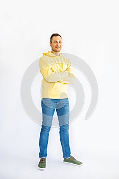 Full length young smiling cheerful man in his 20s wearing yellow hoodie , holding his arms crossed in a folded position